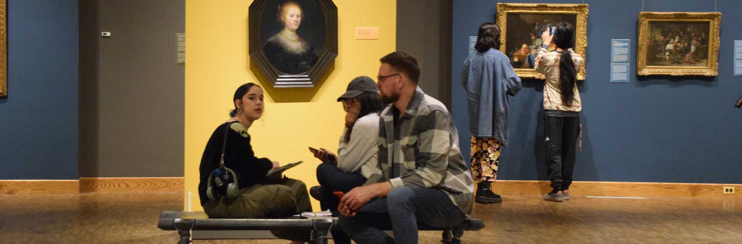 three young adult visitors sitting on a bench in the gallery taking all the art in
