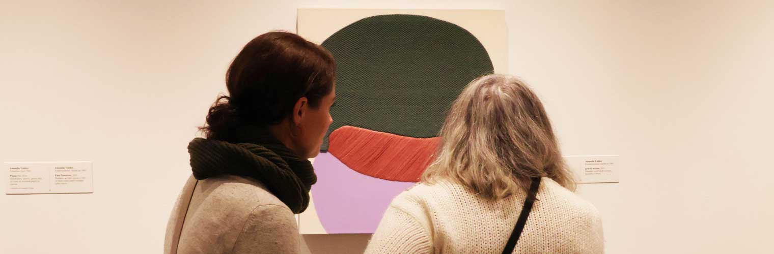 two women looking up close at a modern abstract 2d piece