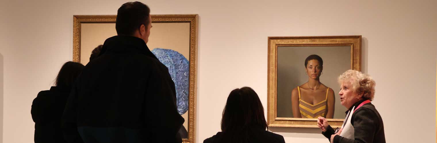 a group of people looking at a painting with a woman talking about it to them