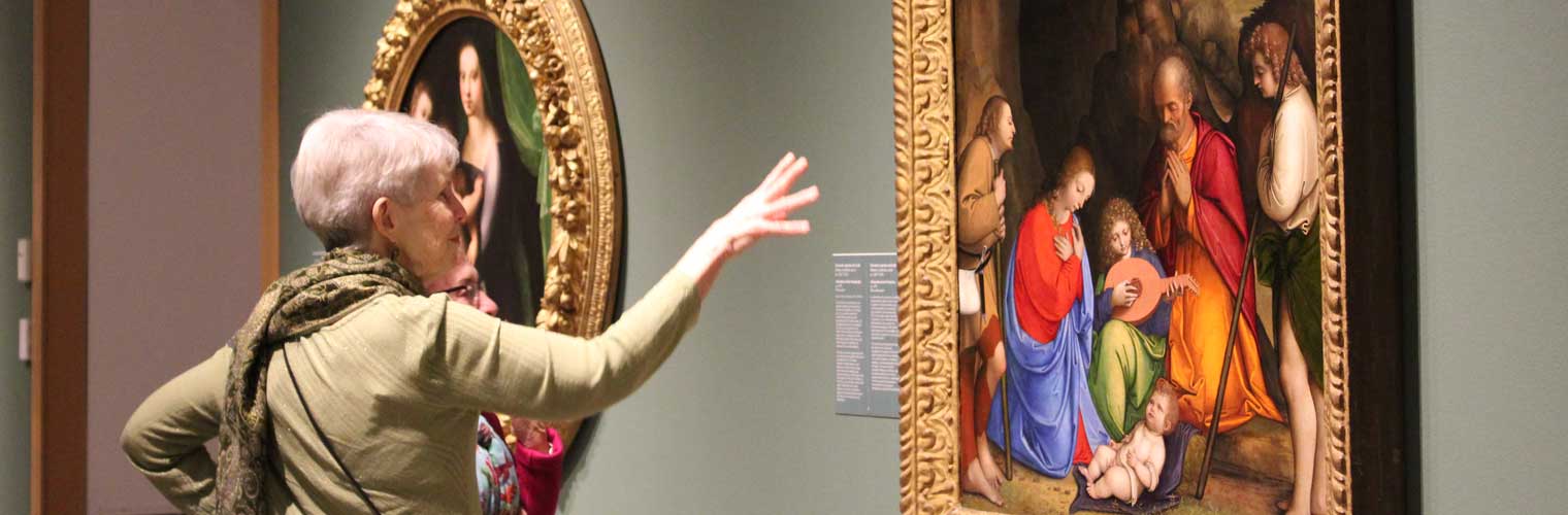 an older woman looking and describing with her hand the scene on the classical painting in a golden frame