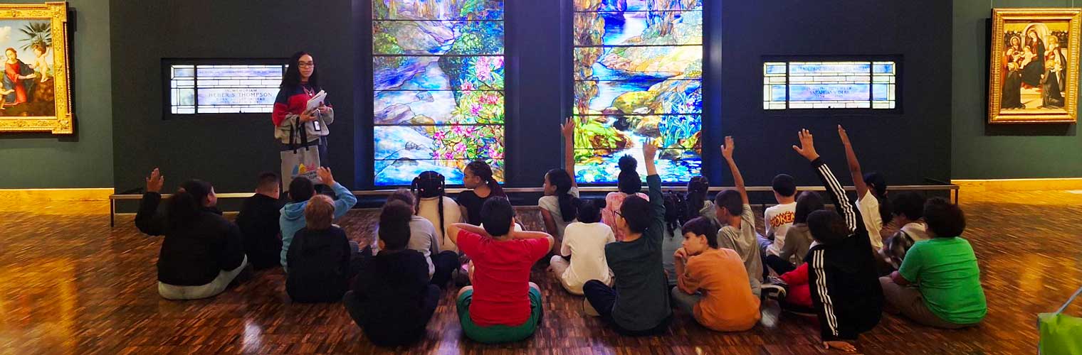 young students sitting on a floor listening to presentation by Tiffany Stained Glass Window