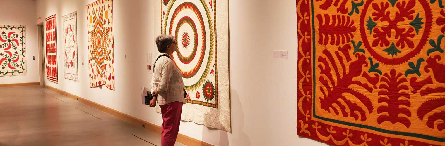 a woman in red pants looking at quilts hanging on a wall